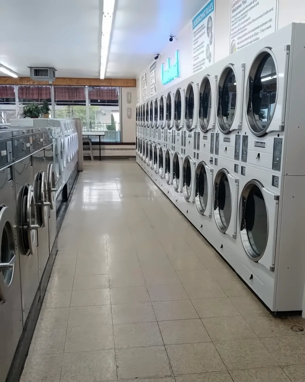 The main aisle at Layton Heights Laundromat, with stainless front-load washers on the left and stacked dryers on the right